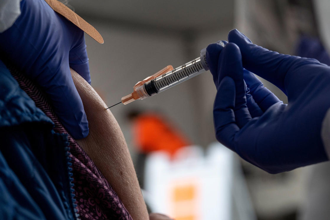 a person holding a baseball bat: A healthcare worker administers a dose of the Moderna Covid-19 vaccine at a walk up vaccination site in San Francisco, California, U.S., on Wednesday, Feb. 3, 2021. San Francisco opened its first neighborhood coronavirus vaccination site in the Mission District on Monday, with plans to open a second in the Bayview in the coming days, reported the San Francisco Chronicle.